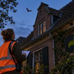vrouw met oranje hesje voor huis in de avond een vleermuis vliegt over